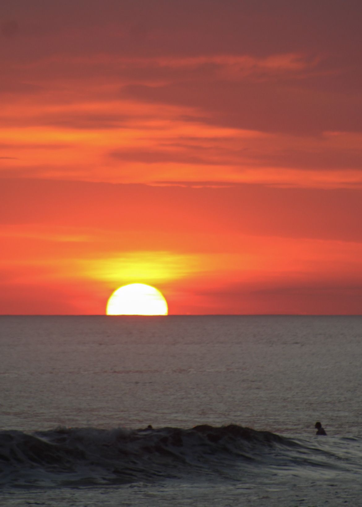 Dramatic red and orange sunset over calm ocean with sun touching horizon.