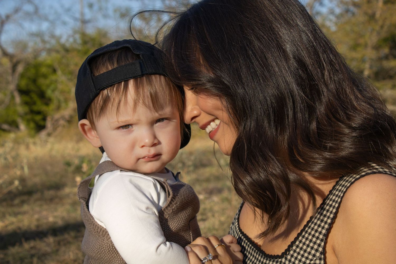 A mother and young child share tender moments outdoors on a sunny day while walking together in nature.