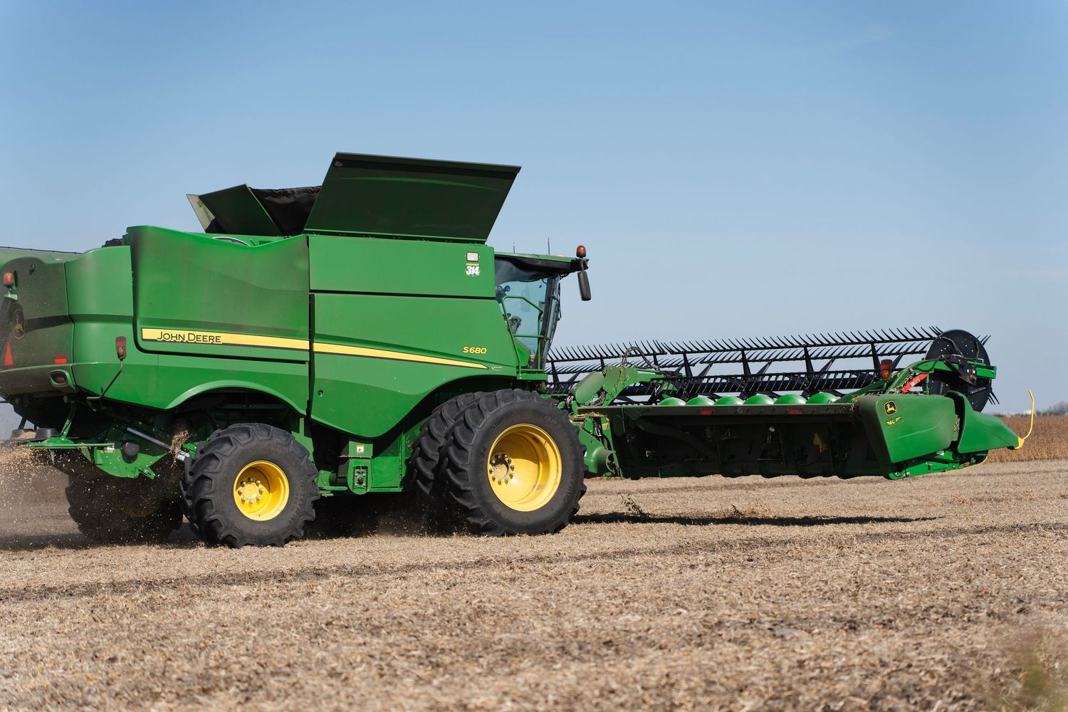 John Deere green combine harvester with header attachment parked in a harvested field under clear blue sky.