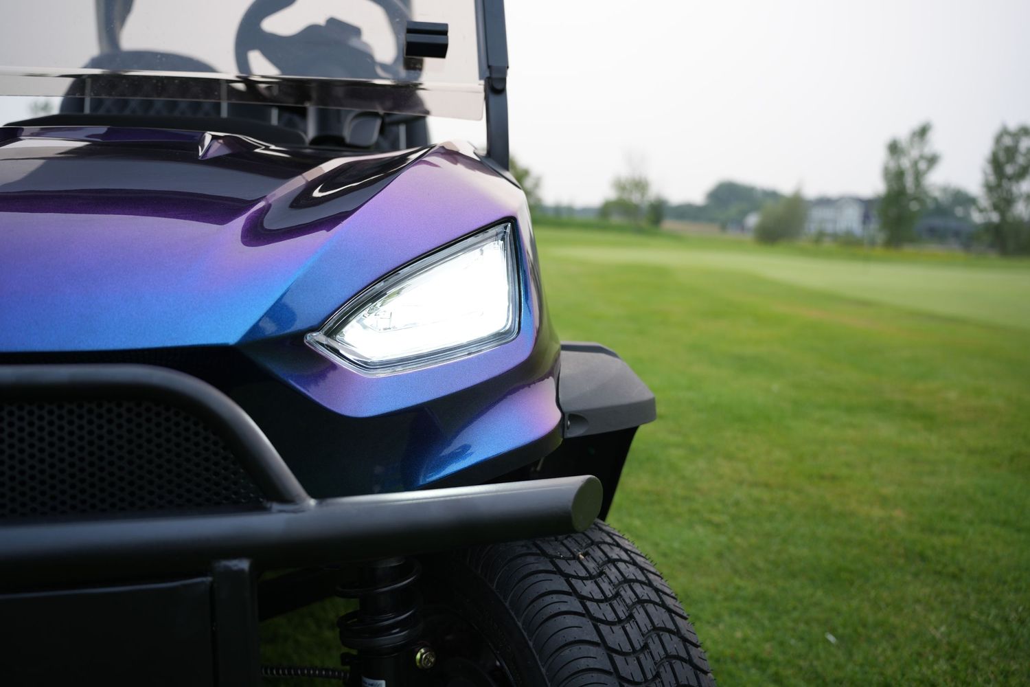 Close-up view of a sleek sports car's headlight detail showing glossy blue paint and aggressive styling elements.
