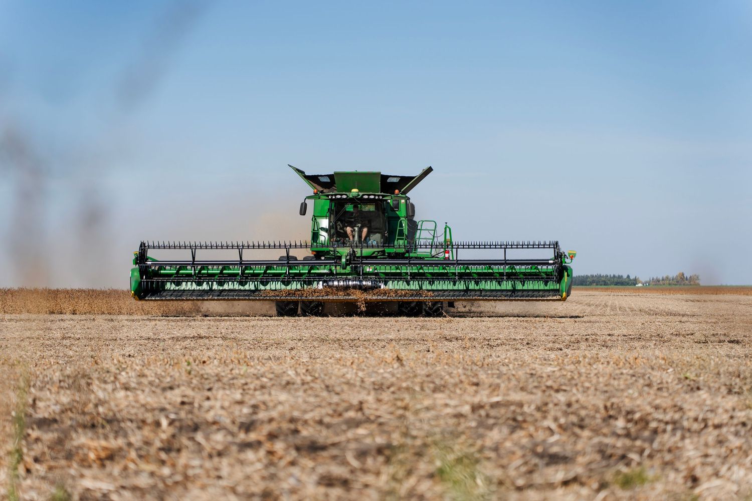 Green combine harvester moving through a dry agricultural field during harvest season.