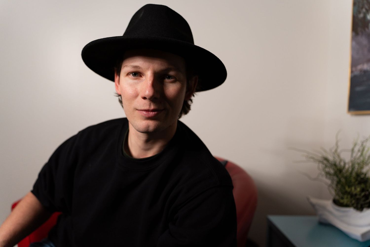 Matt Young wearing a black hat and jacket sits in a dimly lit room with a serious expression.