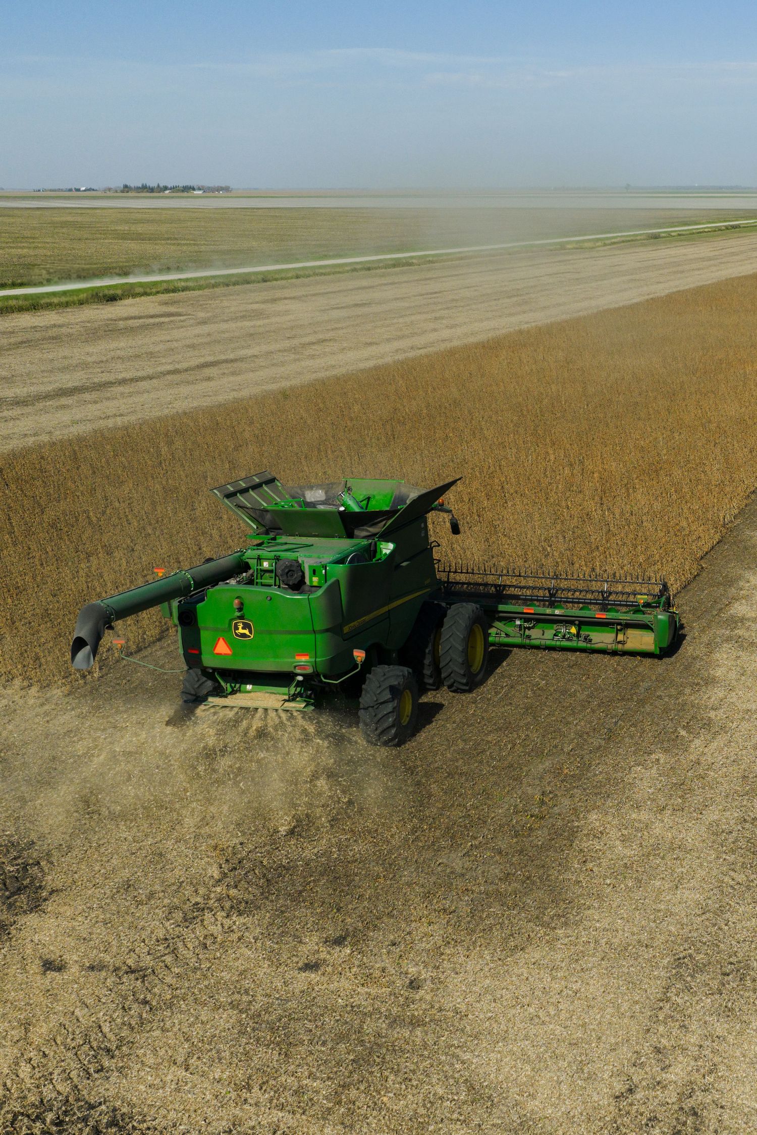 Aerial view of a green John Deere combine harvester working in a vast golden wheat field on a clear day.