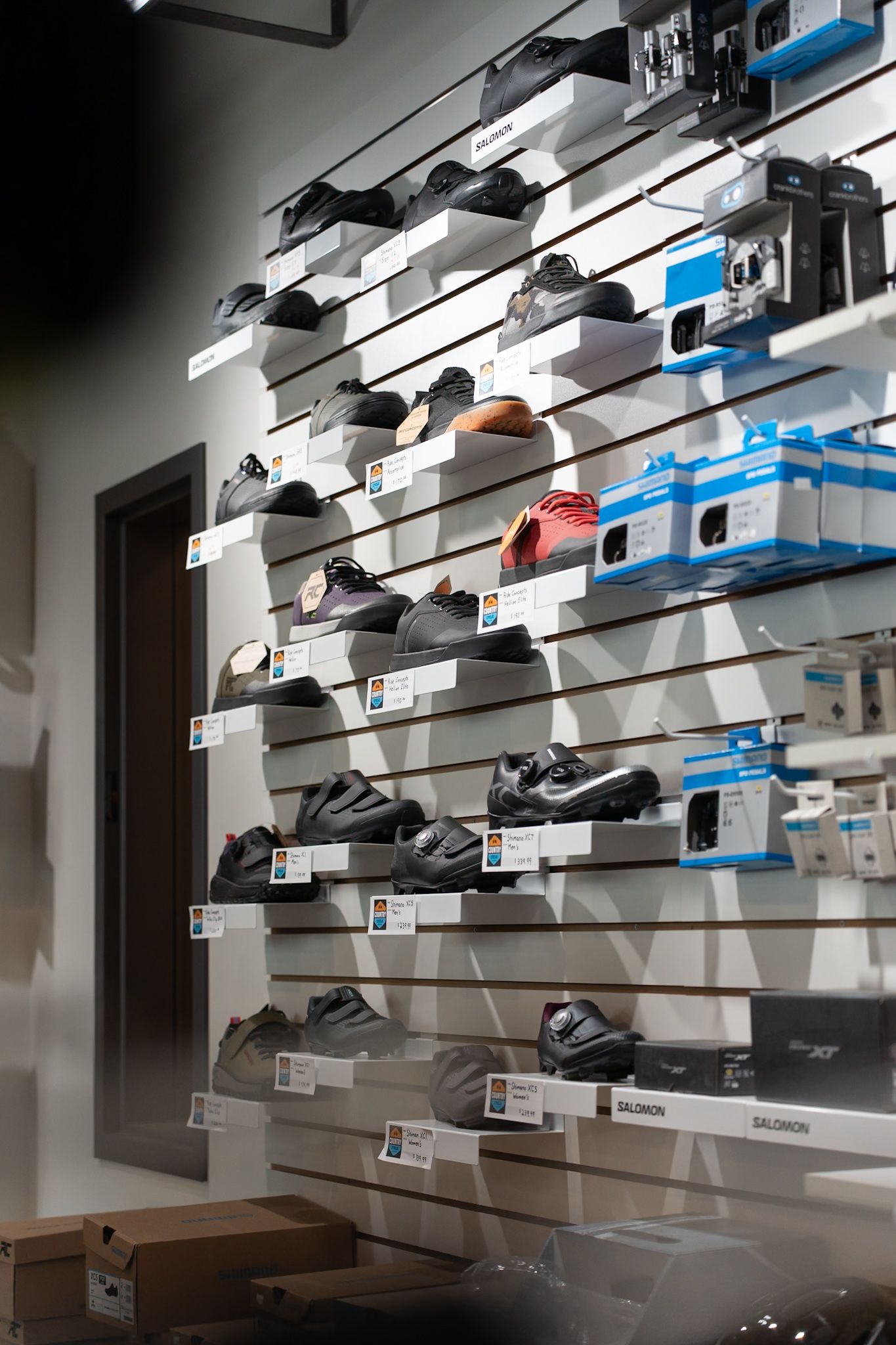 Athletic shoes and sneakers displayed on modern retail wall shelves with bright lighting and price tags.