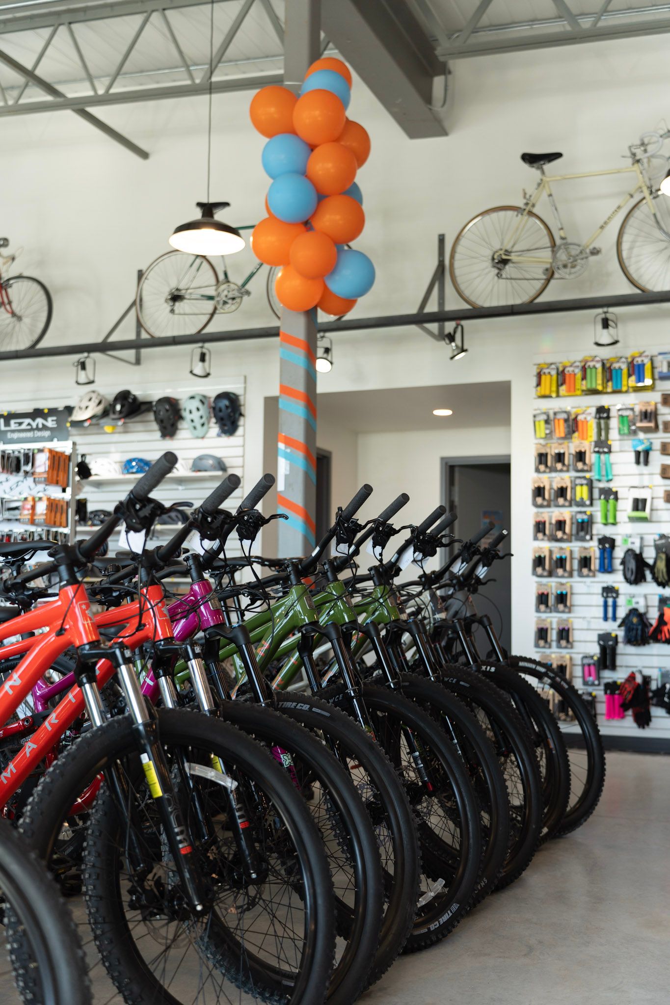 Rows of black and red mountain bikes displayed in a bright bicycle shop with orange and blue balloon decorations.