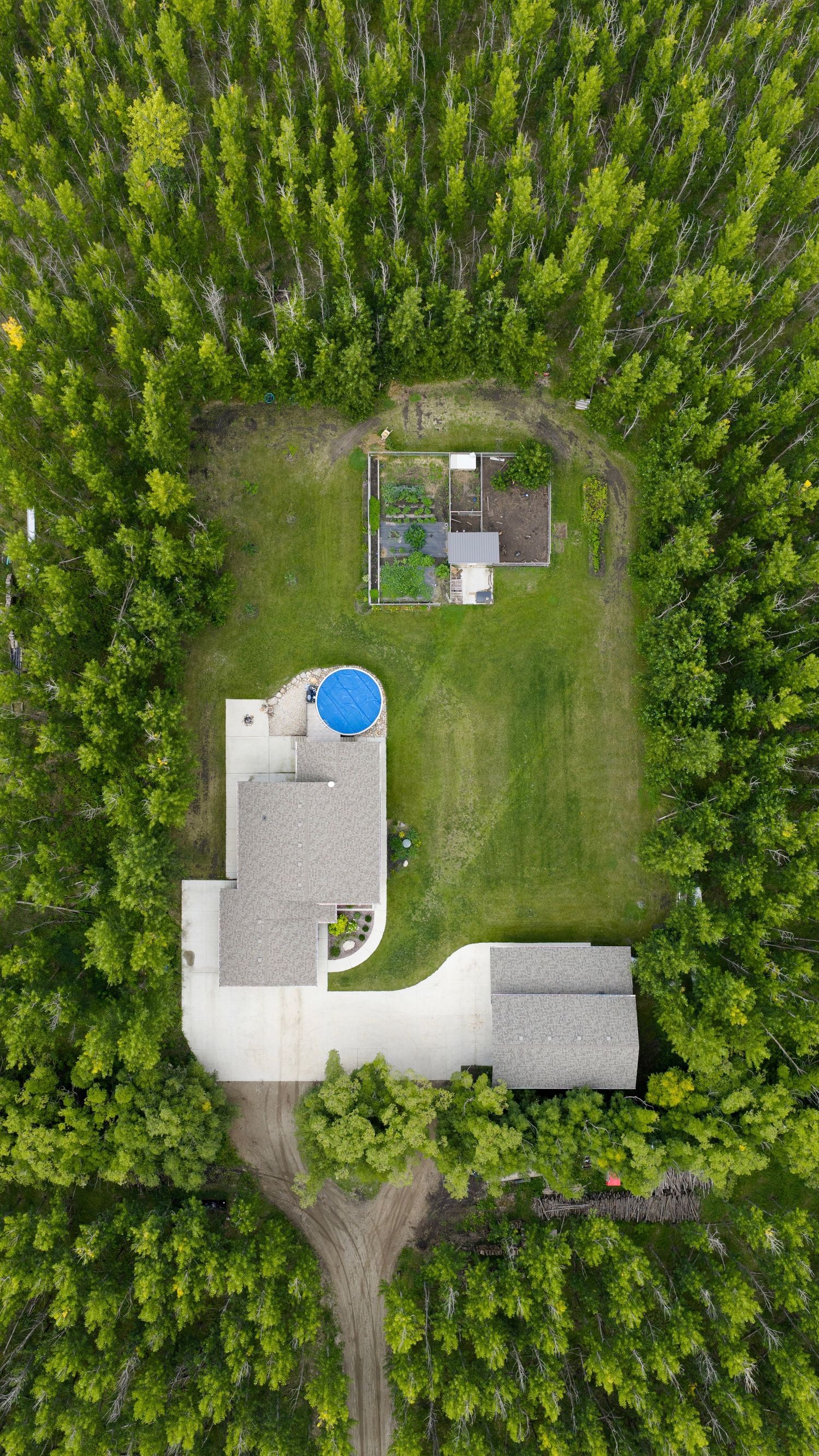 Aerial view of a modern house with a blue swimming pool surrounded by dense green forest and a garden area.