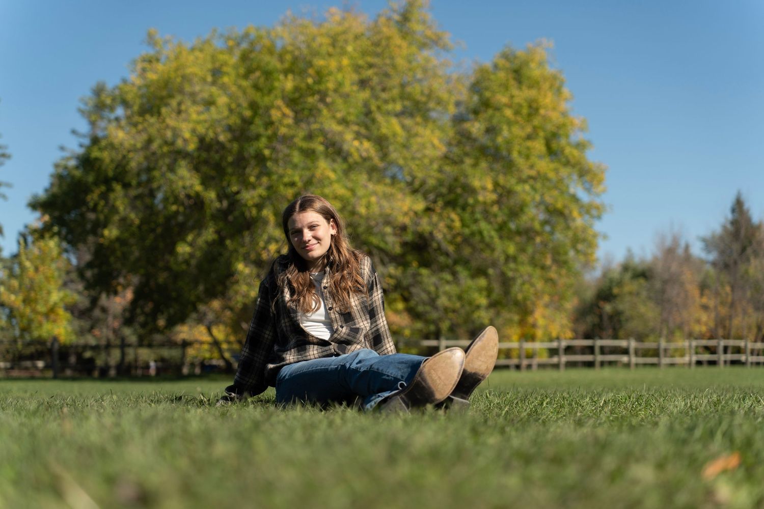 Someone sits on green grass in a park on a sunny autumn day with yellow trees in the background.