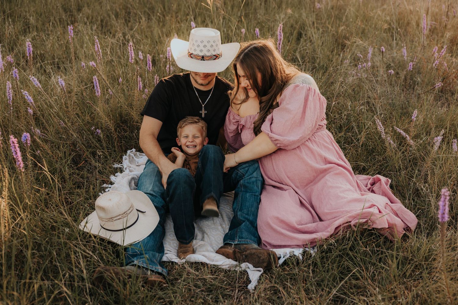 Family enjoying a picnic together in a field of tall grass at sunset.