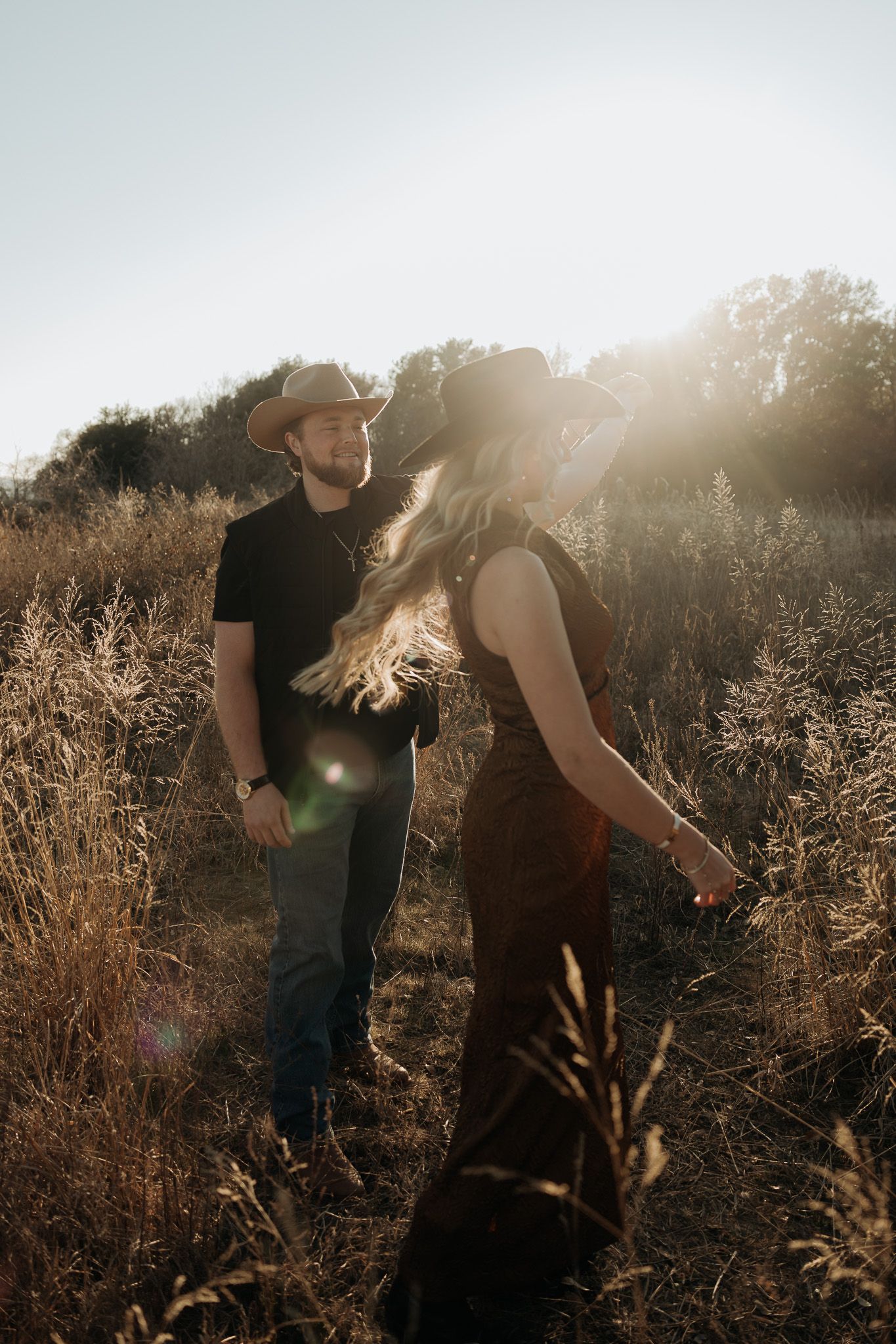 A couple walks through a sunlit field during golden hour as sunflares create a dreamy romantic atmosphere.