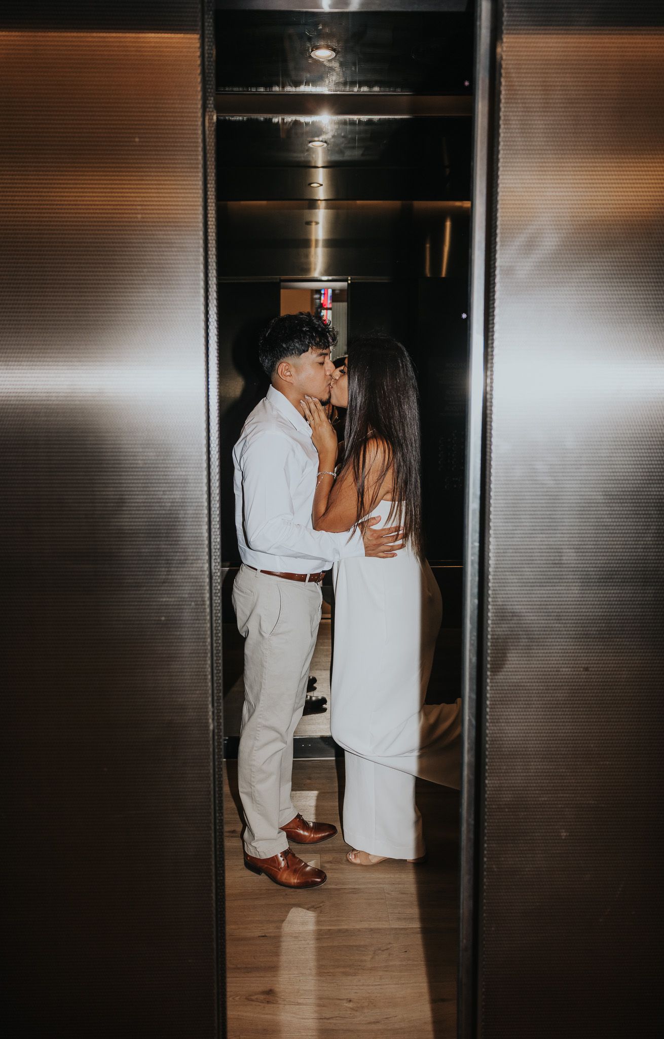 A couple shares an intimate moment in a dimly lit elevator, creating a romantic atmosphere.