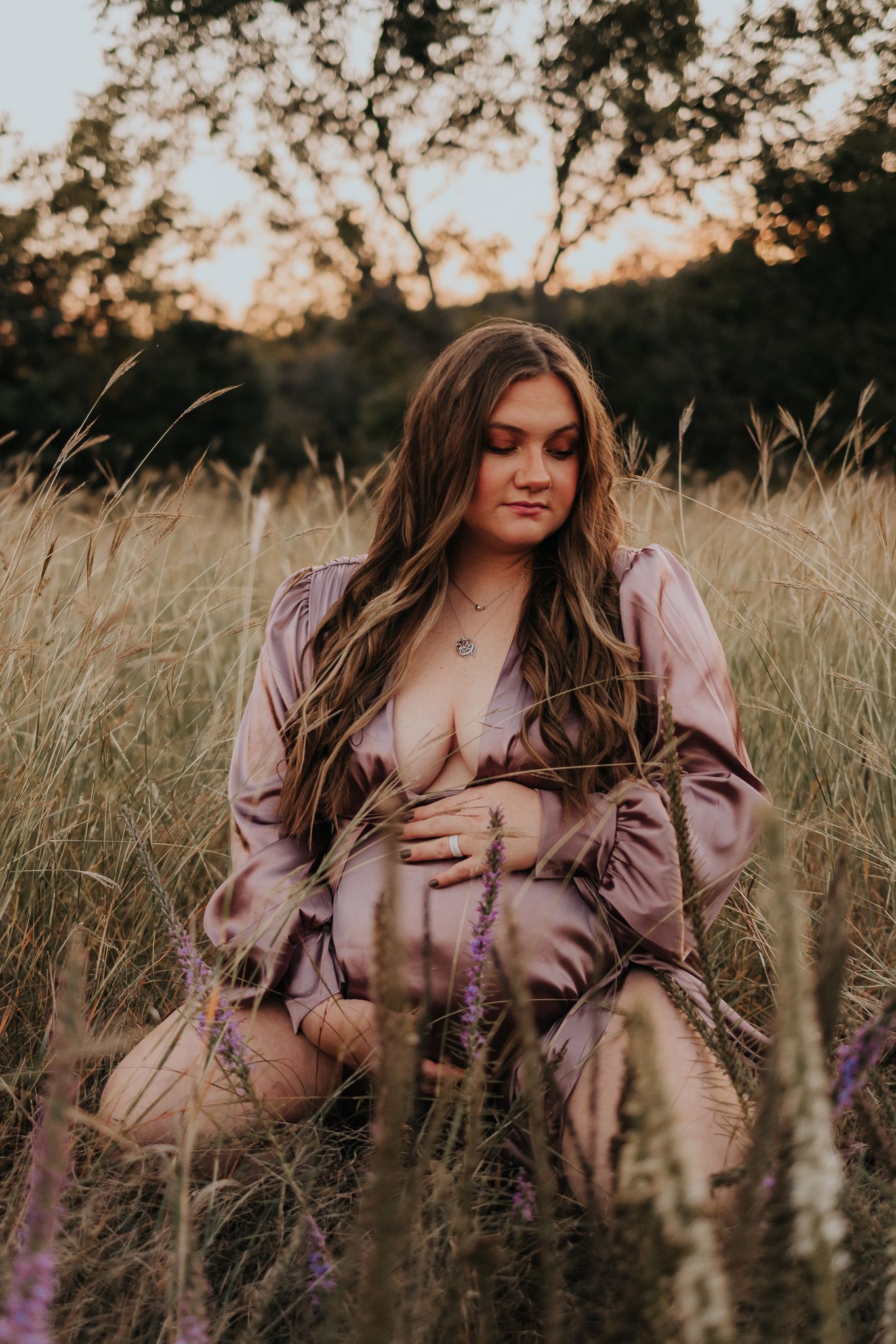 Woman in a mauve dress poses in a golden field with wildflowers at sunset.