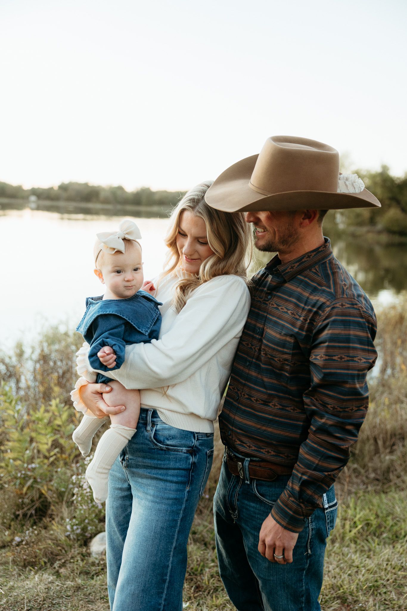 Family in western wear poses together by lake at sunset.