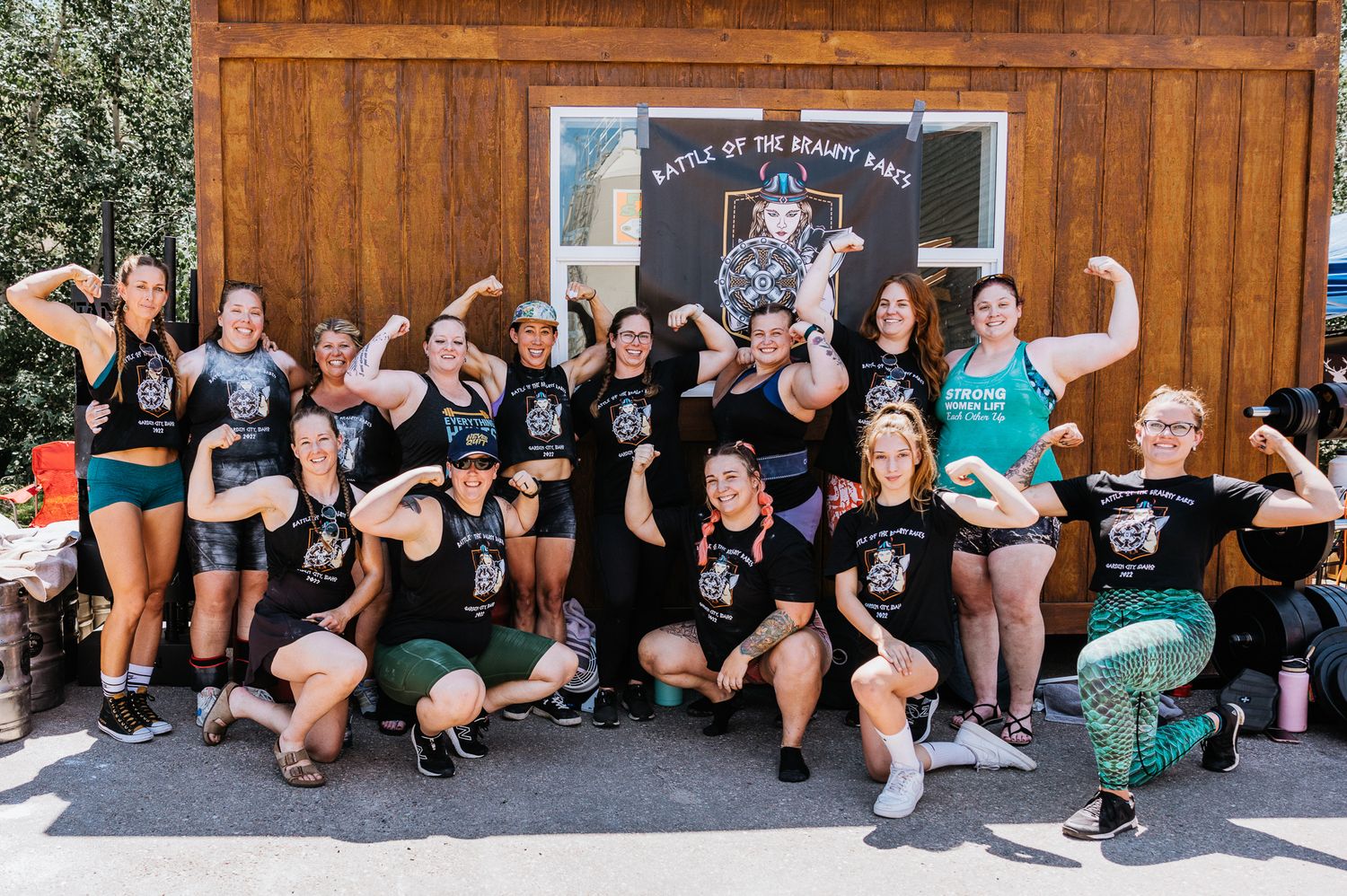 Group of athletes sitting together against a wooden wall at an outdoor competition venue.