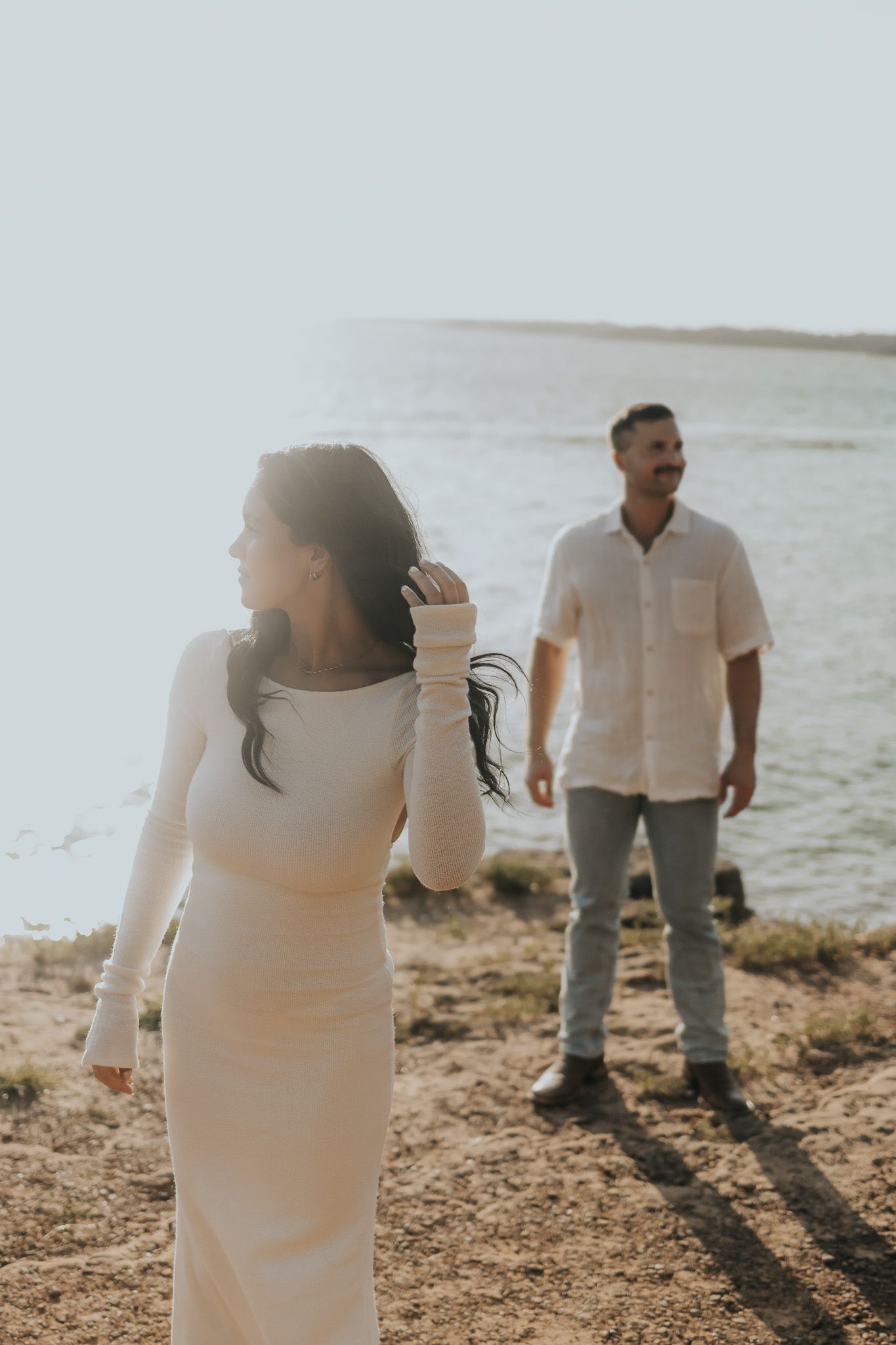 A romantic couple shares tender moments together during a sunset photoshoot on a beach shoreline.