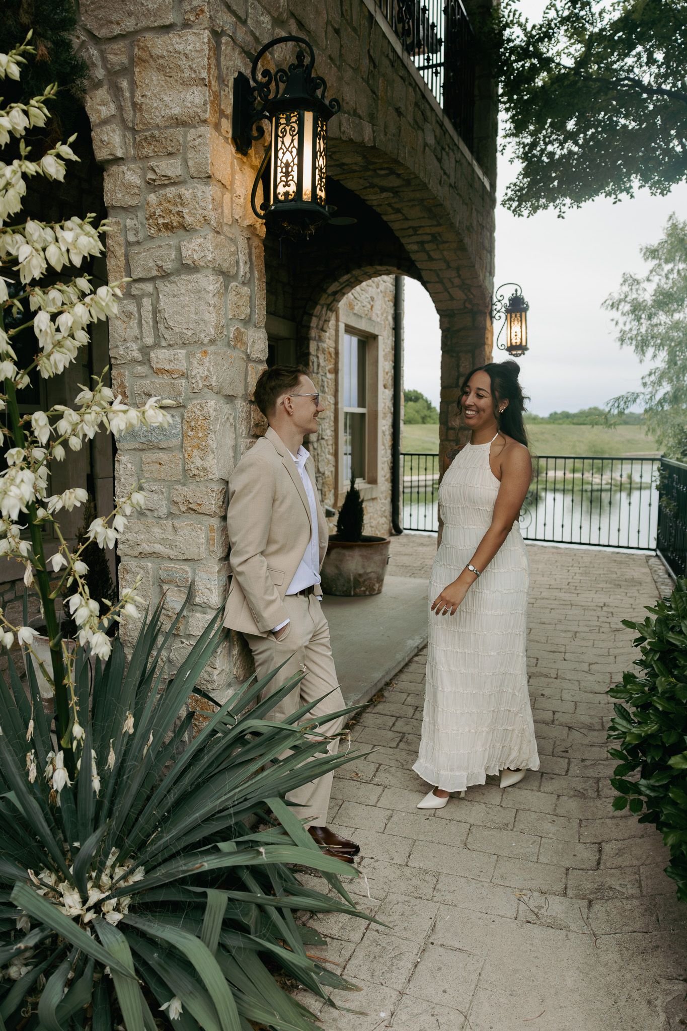 Couple in wedding attire sharing a joyful moment on a stone patio with arched doorway and lush greenery.