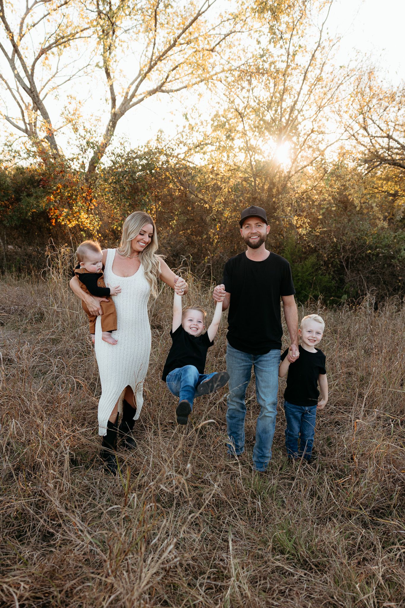 Family of five posing together in tall grass during golden hour sunset photoshoot.