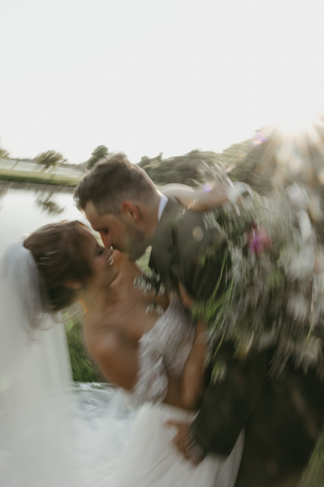 Artistic motion blur photo captures newlyweds sharing their first kiss at sunset.