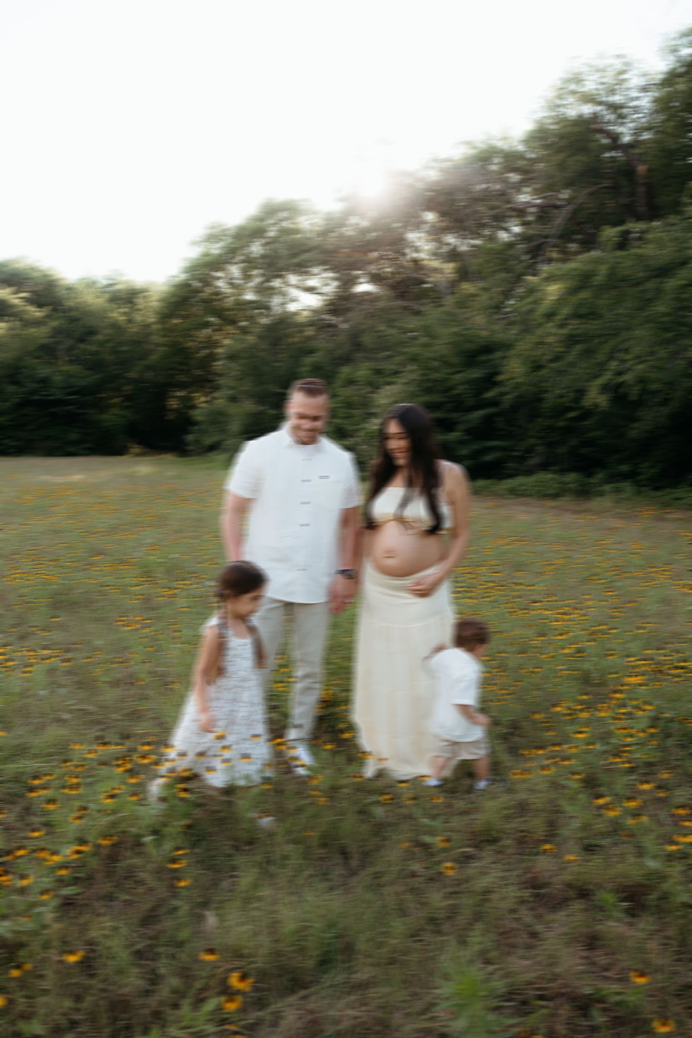 Pregnant woman in white dress with family in flower field.