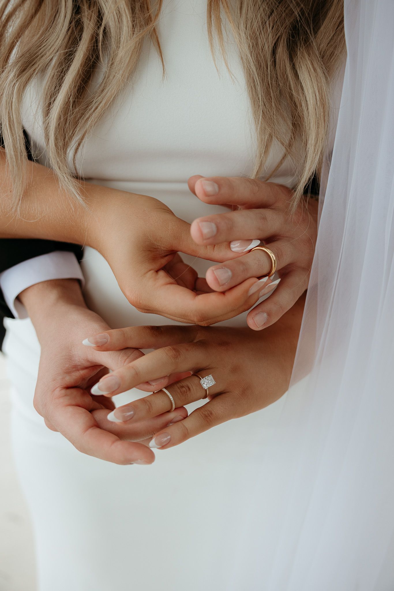 Close-up detail shot of hands with wedding rings against white fabric background.