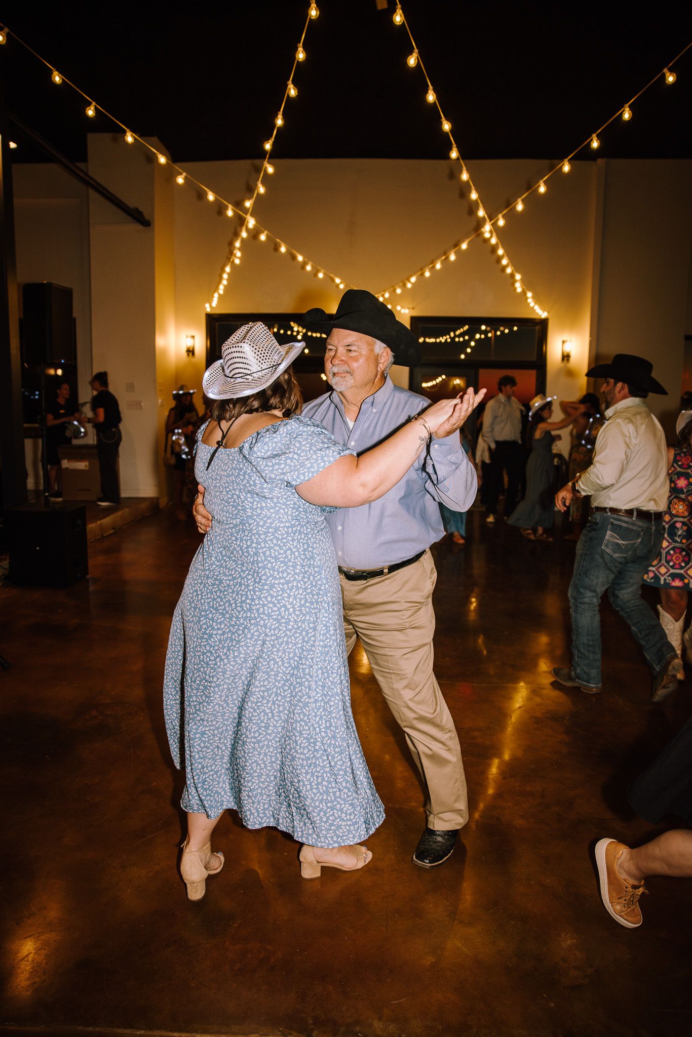 Couple dancing in cowboy hats at a country wedding reception with string lights.