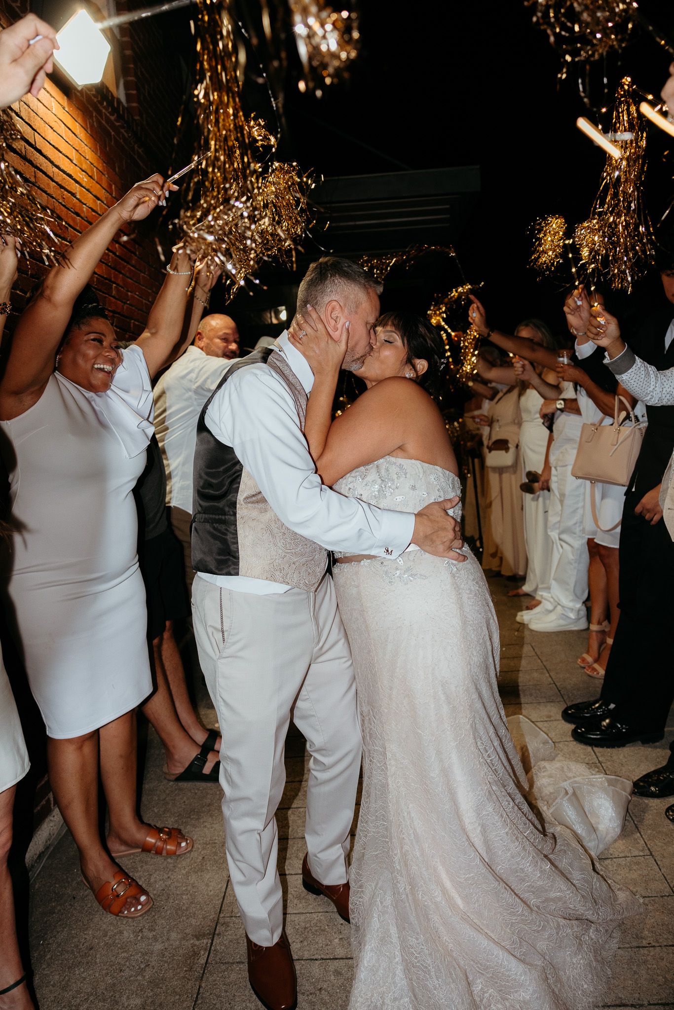 Wedding reception dance floor filled with guests in white attire under glittering lights.
