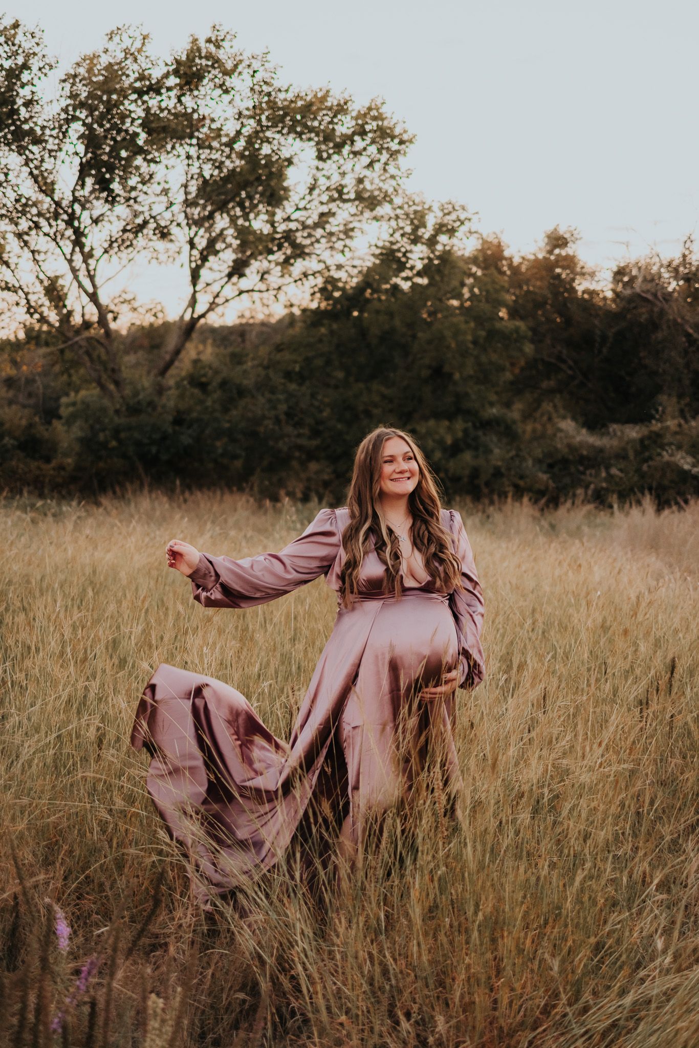 Person in pink dress twirling gracefully through a sunlit field of tall grass at golden hour.