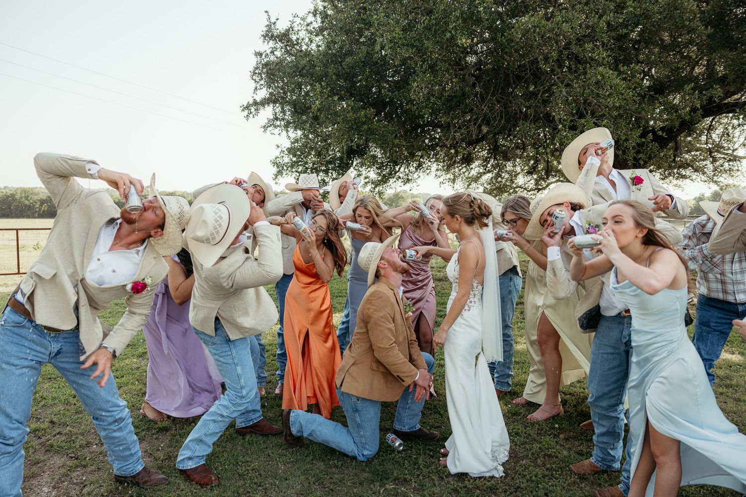 Wedding party jumps in synchronized pose wearing casual western attire against natural backdrop.
