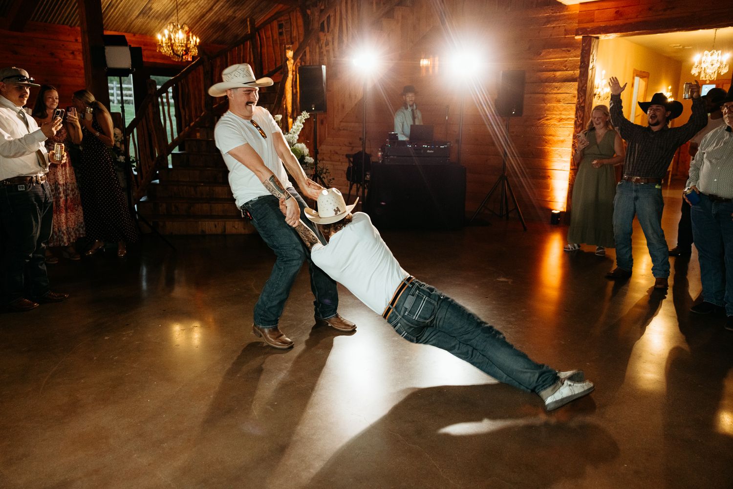 Couple dancing at a rustic wedding reception, groom in cowboy hat dipping partner on dance floor.