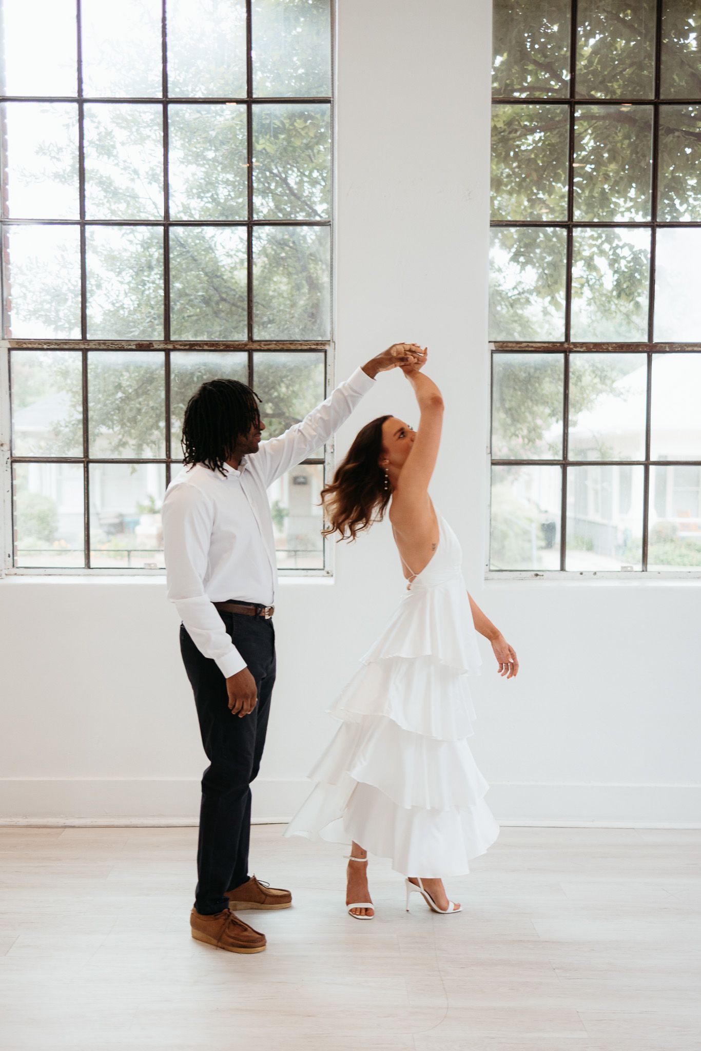 A couple dances together in a bright white studio with large windows, creating a romantic and ethereal atmosphere.