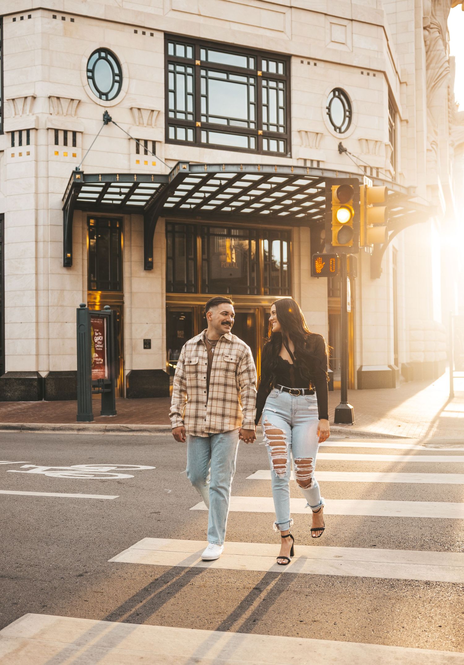 Couple walking down a sunlit city street with classic architecture in the background.