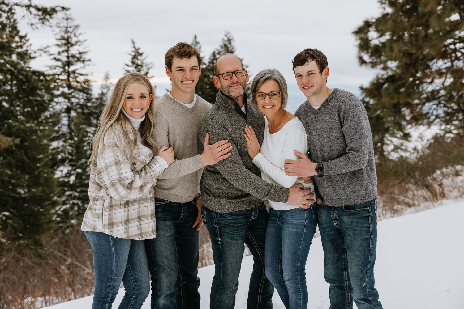 A family wearing coordinated grey and white outfits poses together in a snowy winter setting.