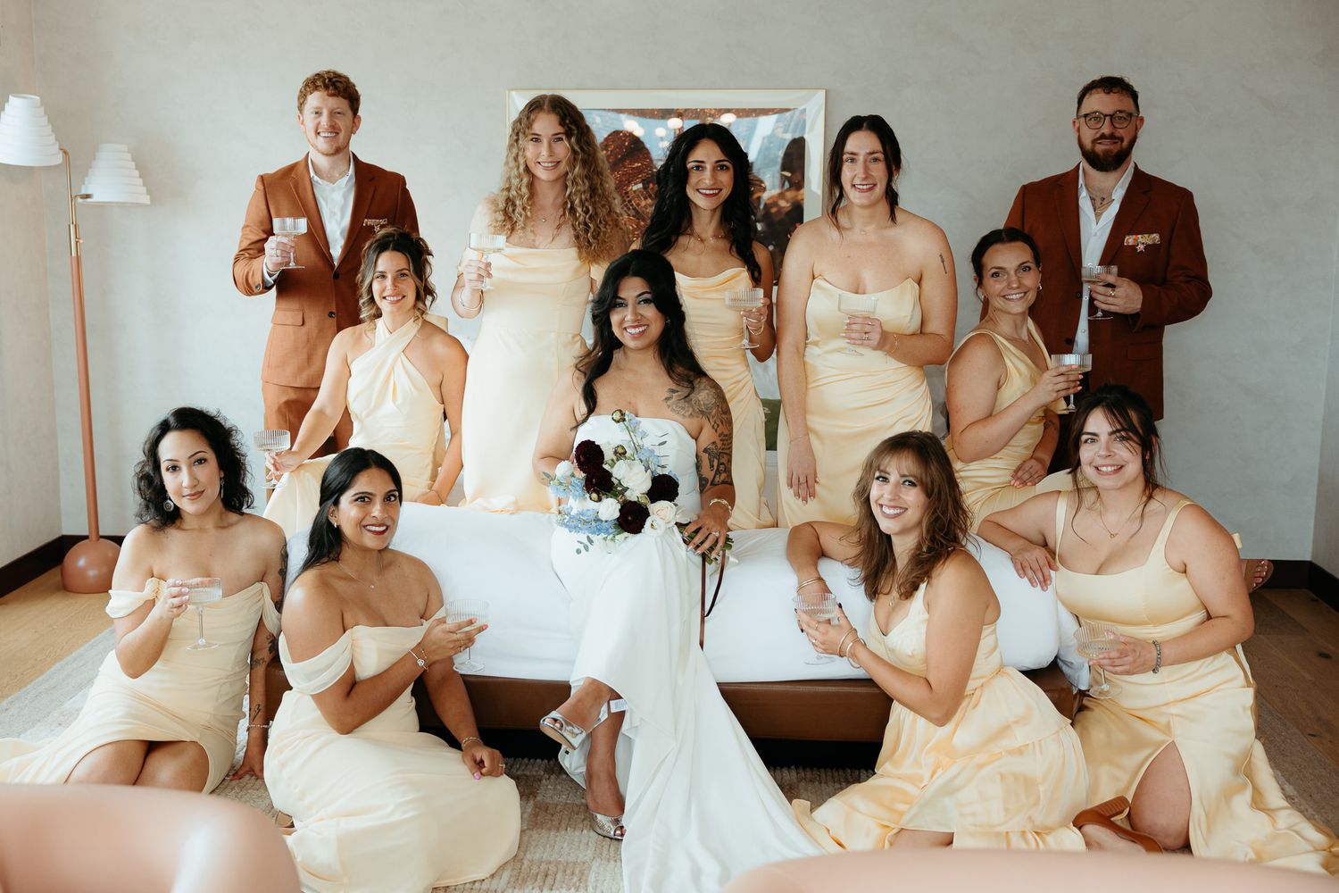 Bride in white gown poses with bridesmaids in yellow dresses and groomsmen in brown suits at a wedding celebration.