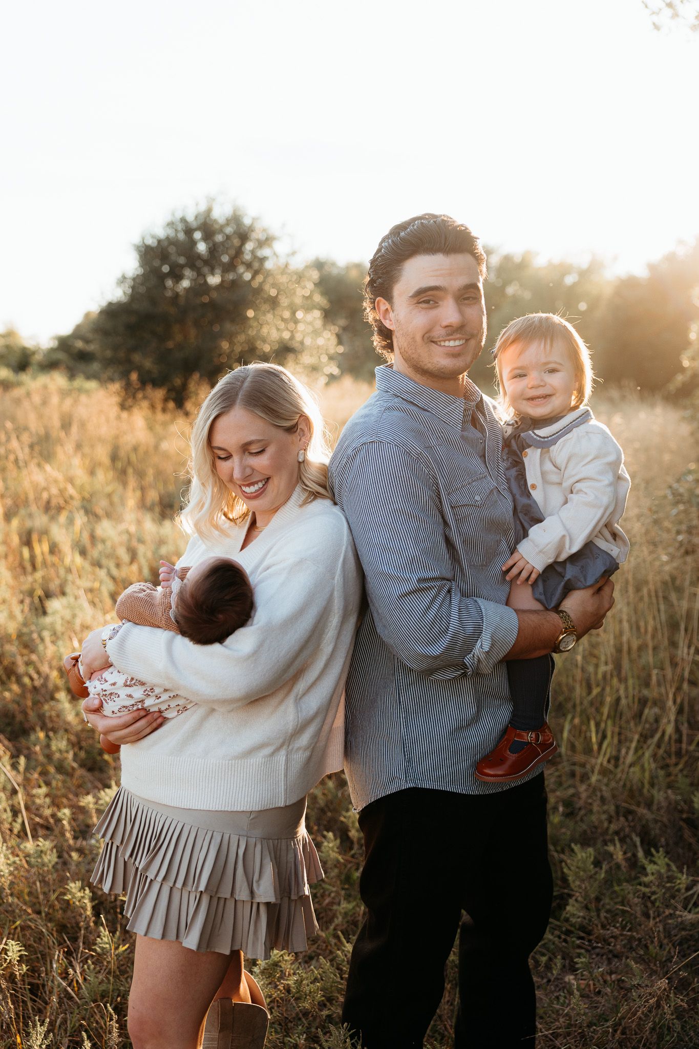 Family portrait in golden sunset light among tall grass in field.