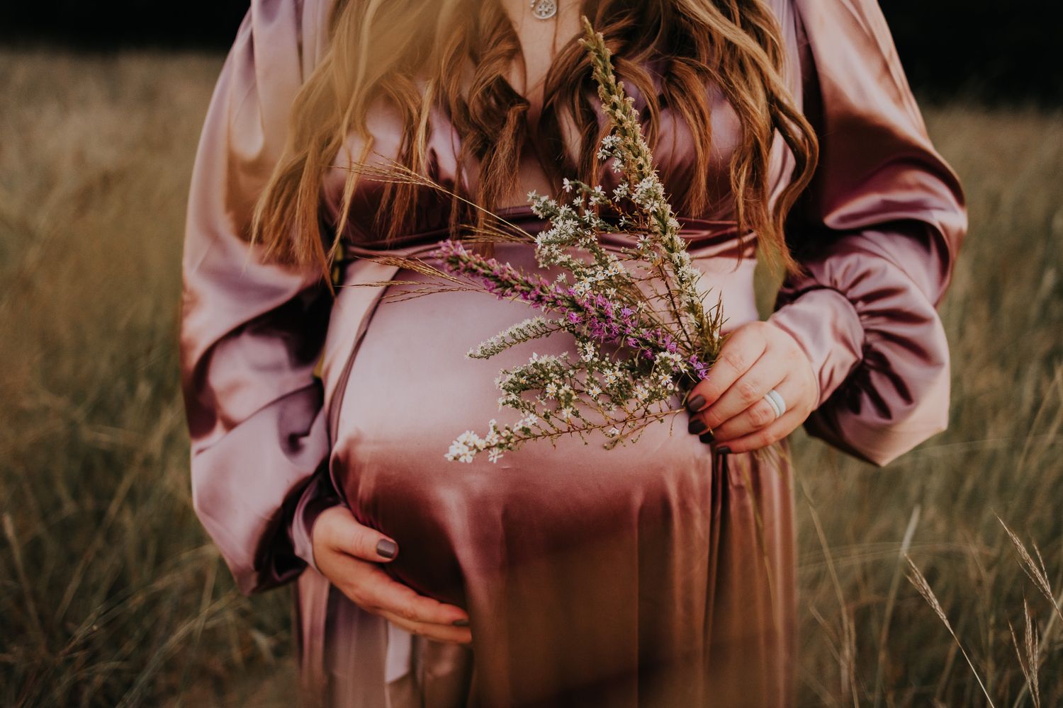 Pink dress and brown leather bag against dark background in rustic outdoor setting.