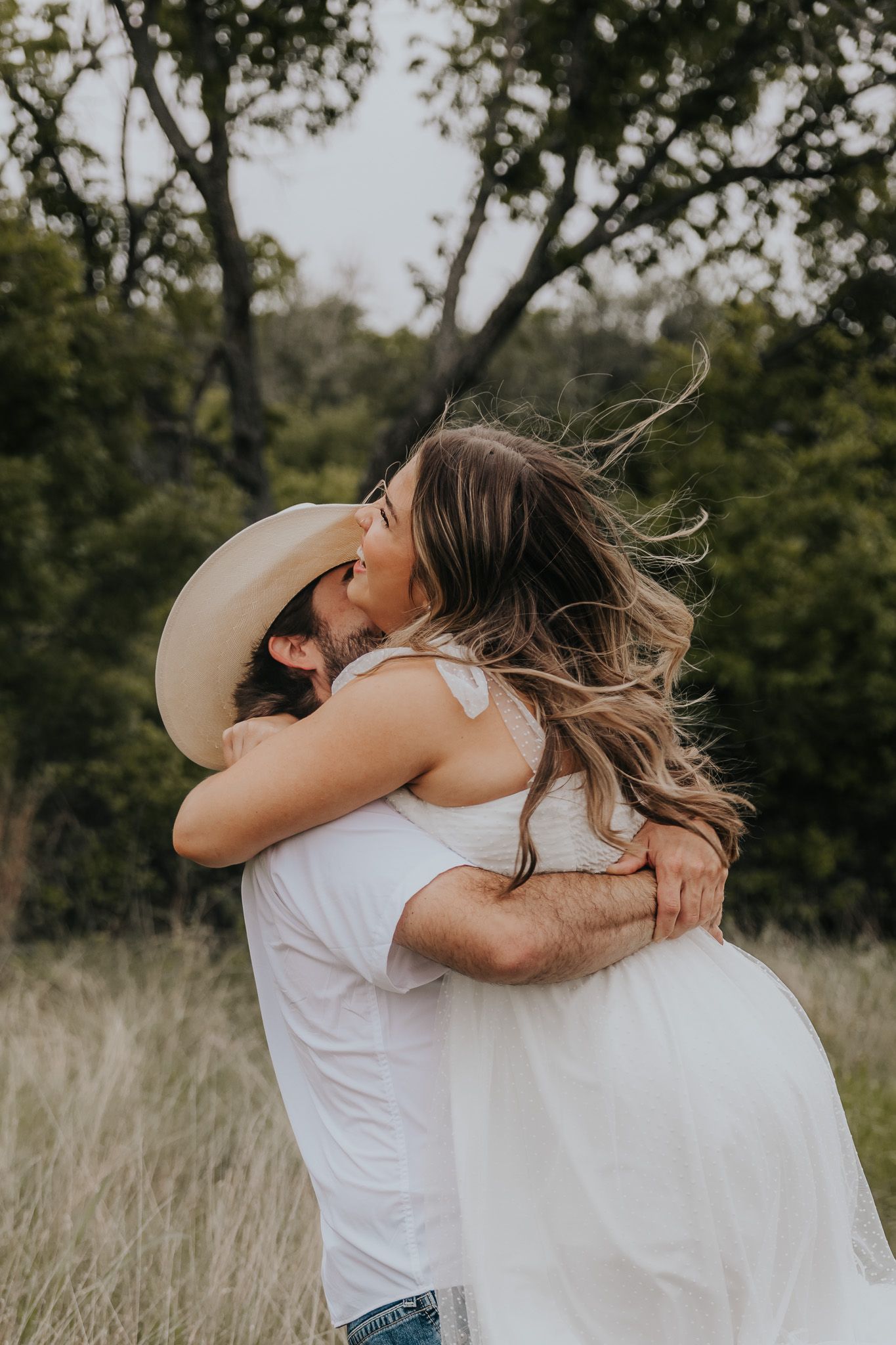 A romantic couple in white outfits embrace in a sun-lit field of tall grass.