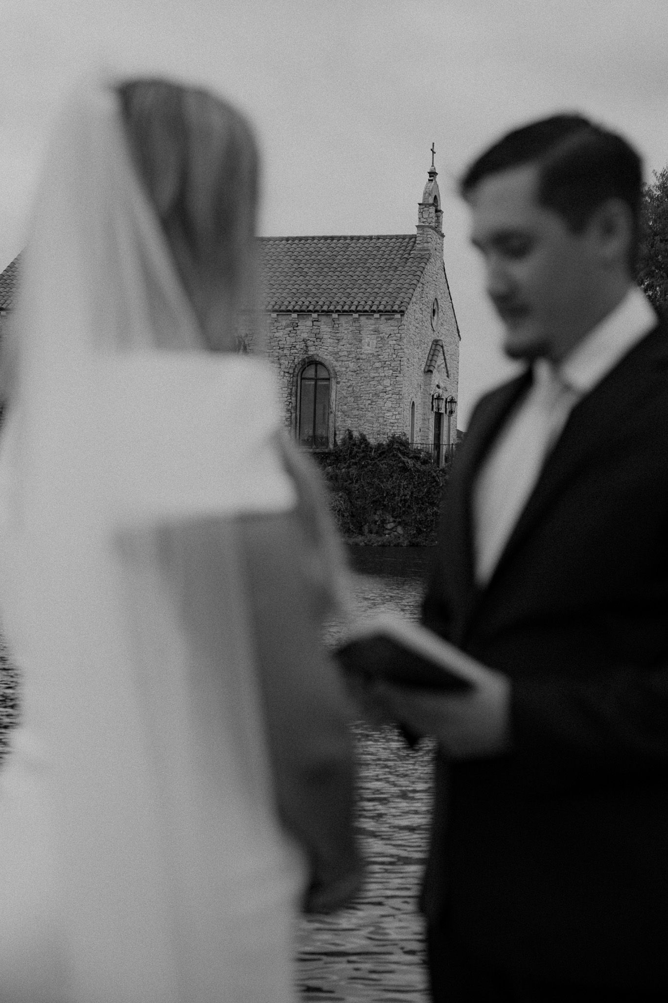 Black and white wedding photos showing a couple by a waterfront stone building.