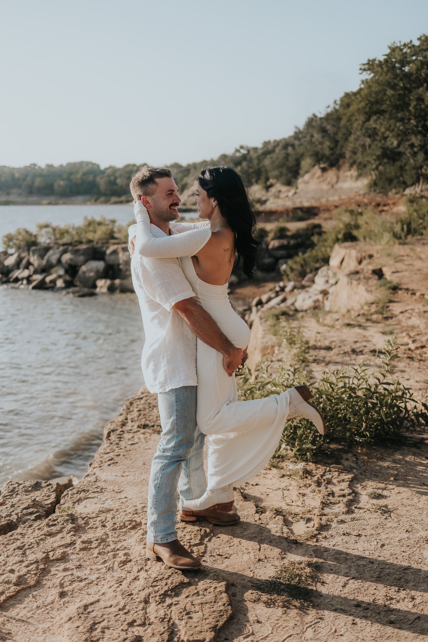 A romantic couple dances together on a rocky beach shoreline at sunset.