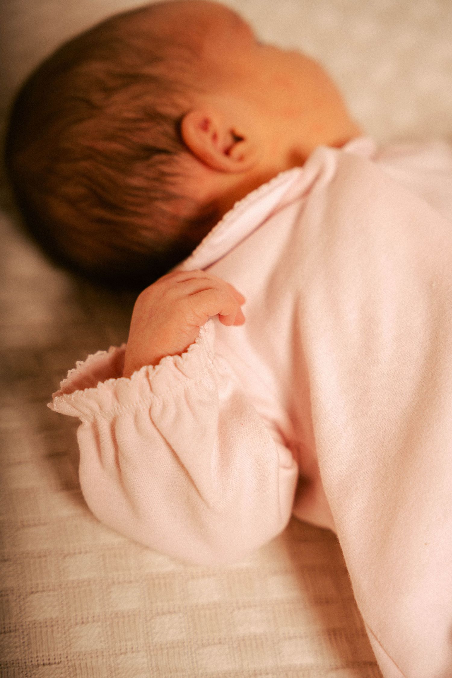 A sleeping baby wearing soft pink clothing rests peacefully on textured fabric.