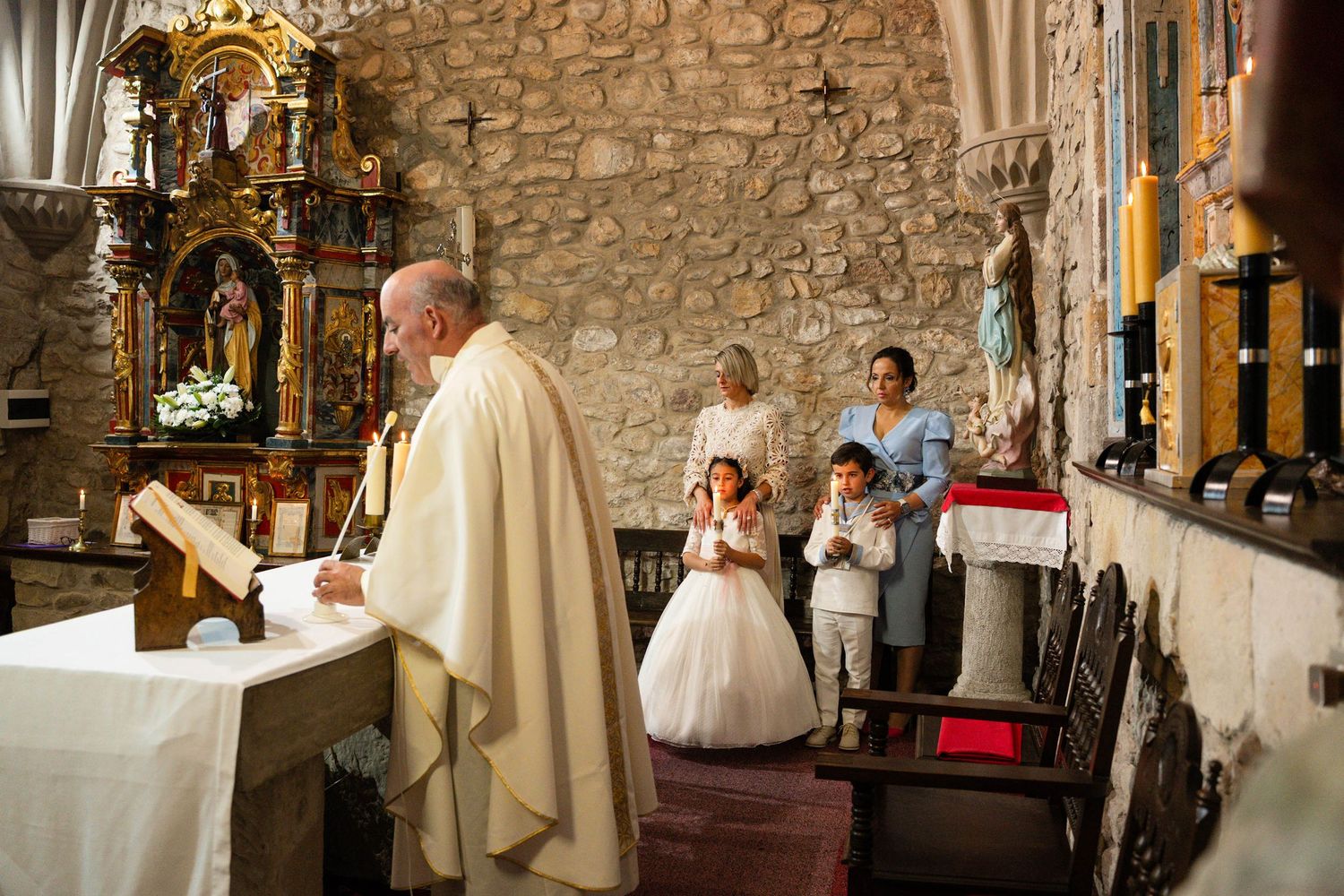 A priest conducts a religious ceremony at a stone church altar with a white cloth.