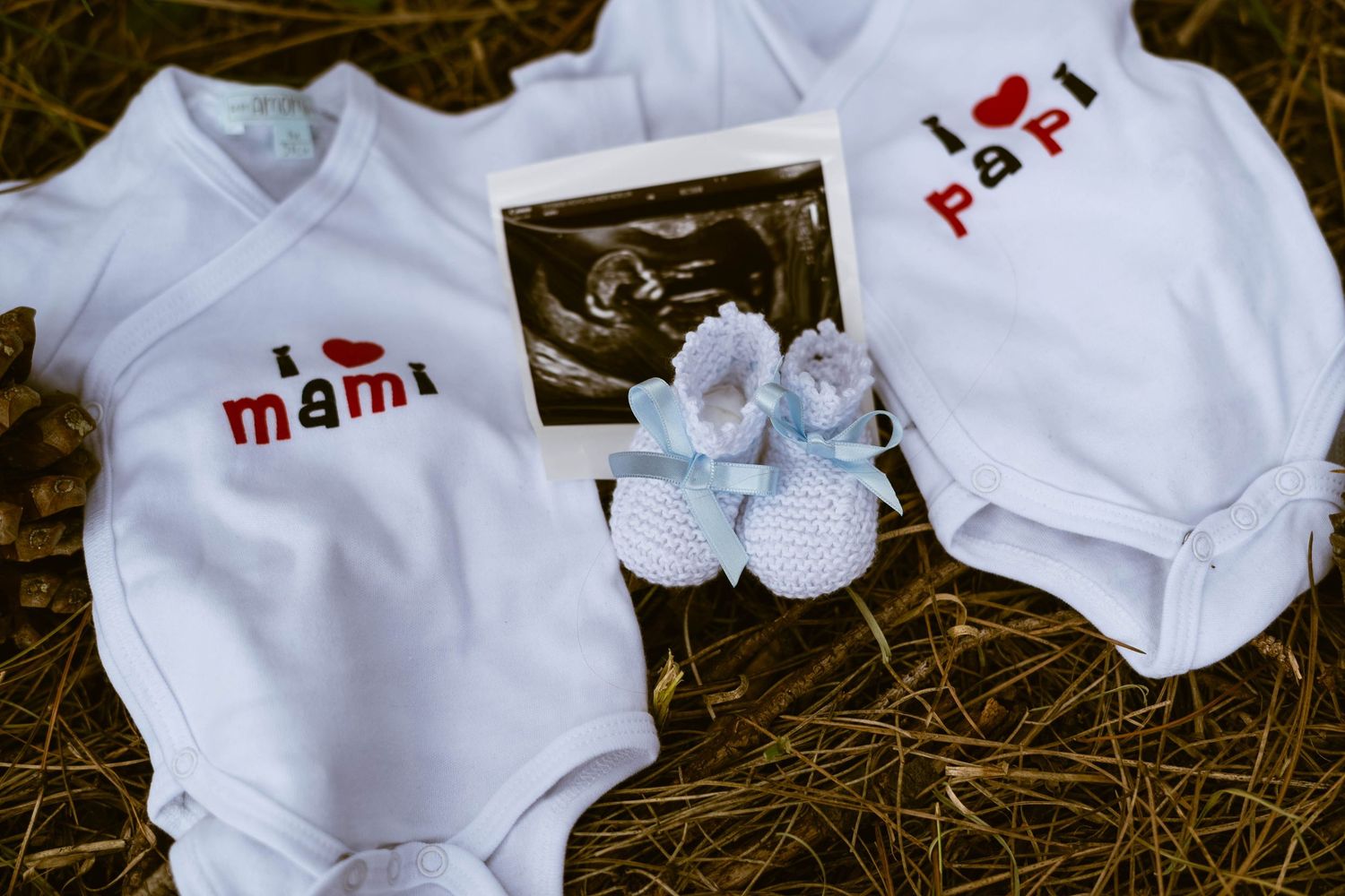 White baby clothes and accessories arranged on a rustic wooden surface.