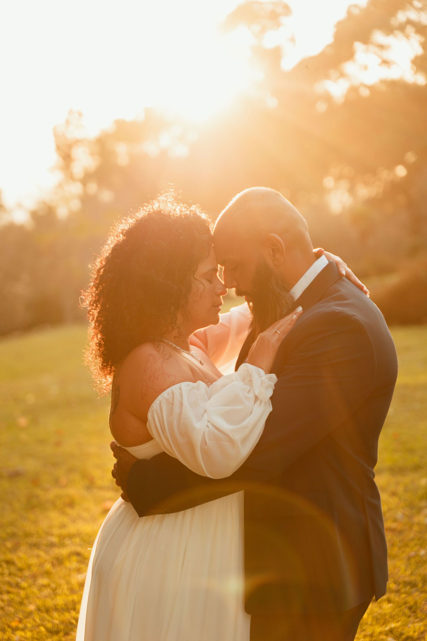 A couple embraces during golden hour sunset in an outdoor wedding photo.