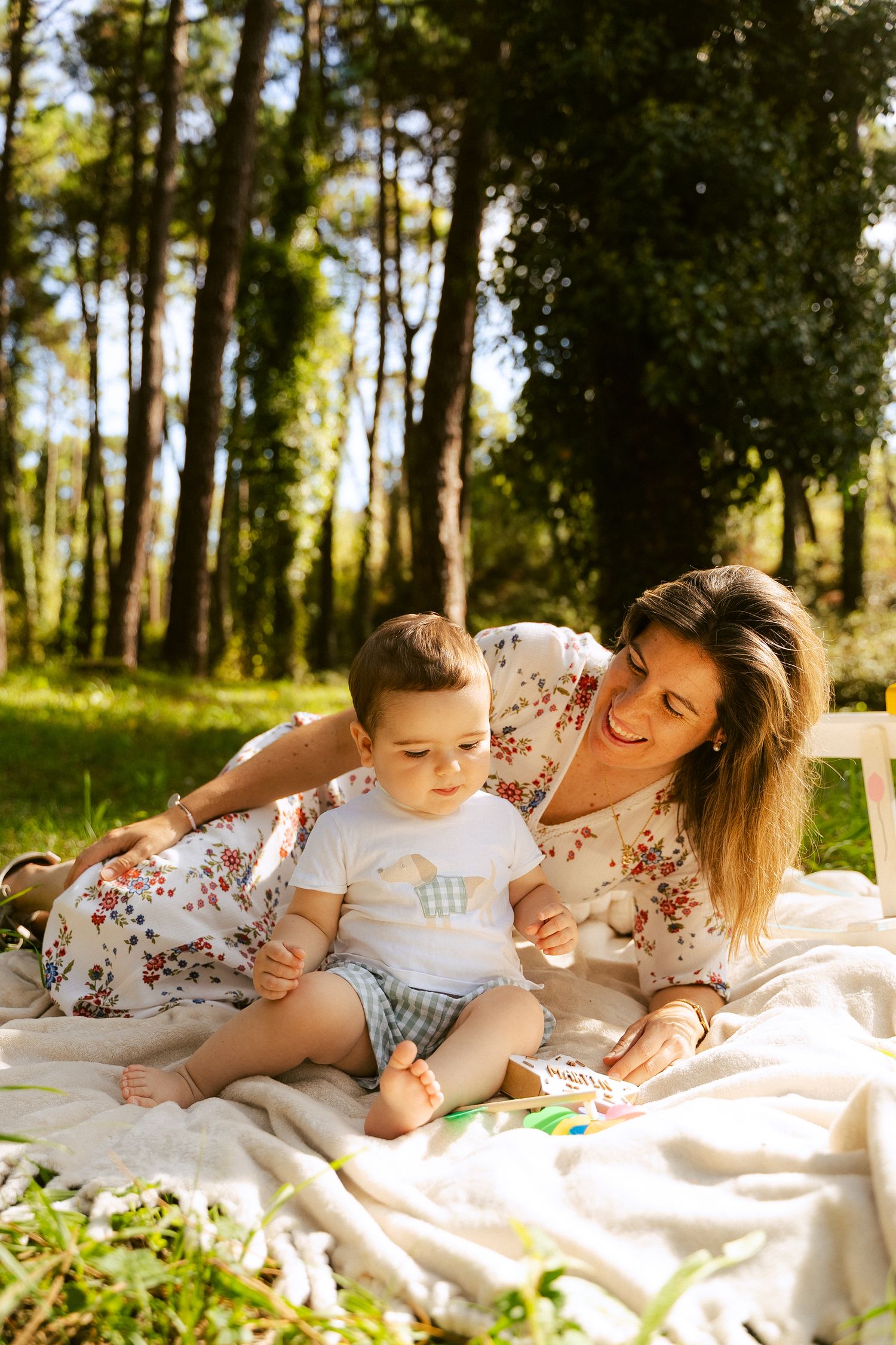 Intimate family playtime captured on a blanket during an outdoor photoshoot in a wooded area.