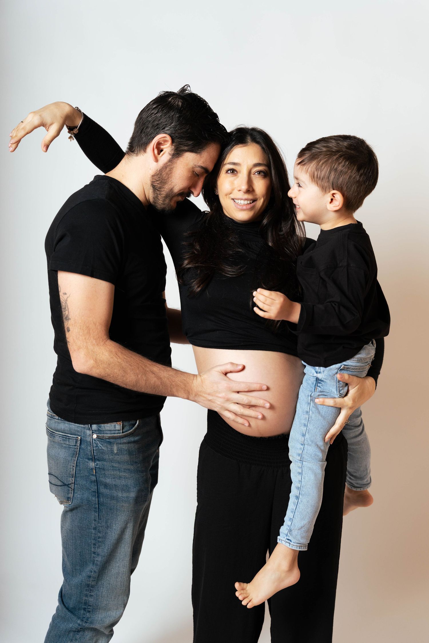 A maternity photo series showing a couple and child in black and white outfits against a light background.