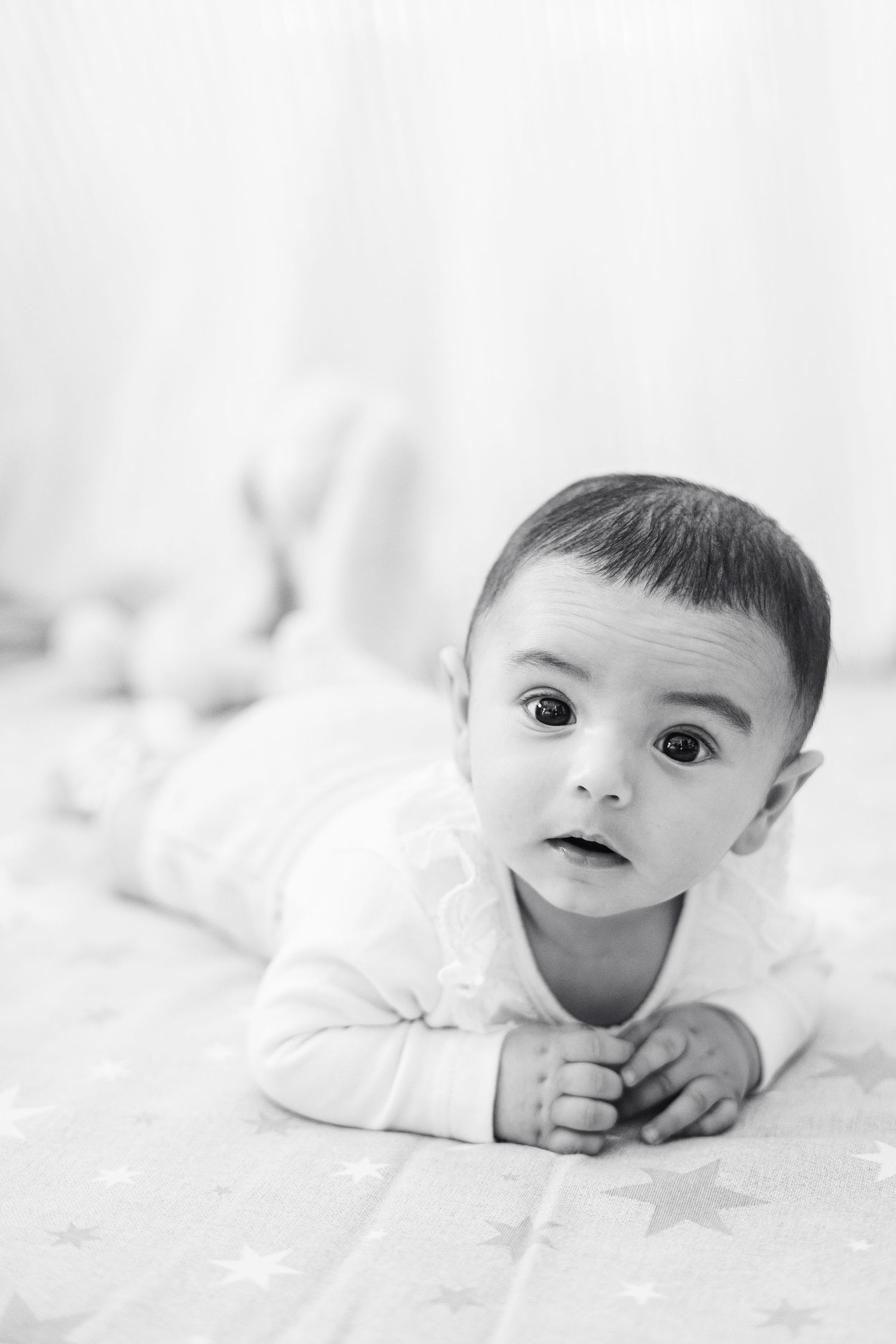 A series of black and white portraits showing a baby lying on white bedding in different poses.