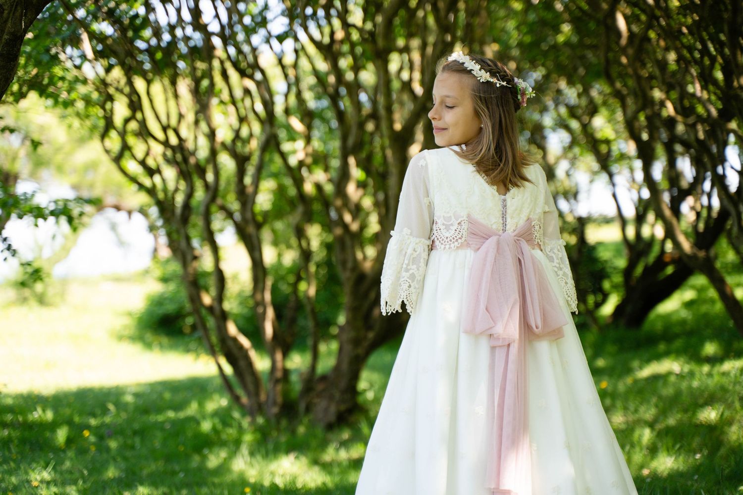White dress with pink bow sash photographed in a sunlit garden setting.