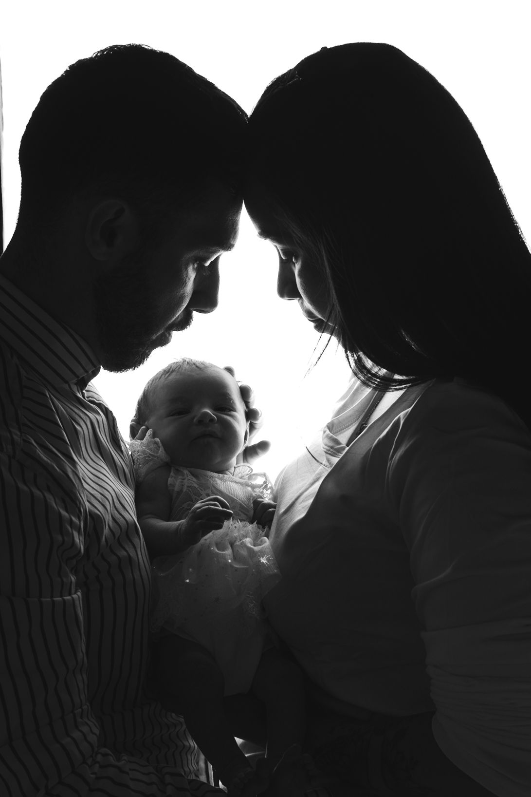Black and white silhouette of parents holding their smiling baby in an intimate family portrait.