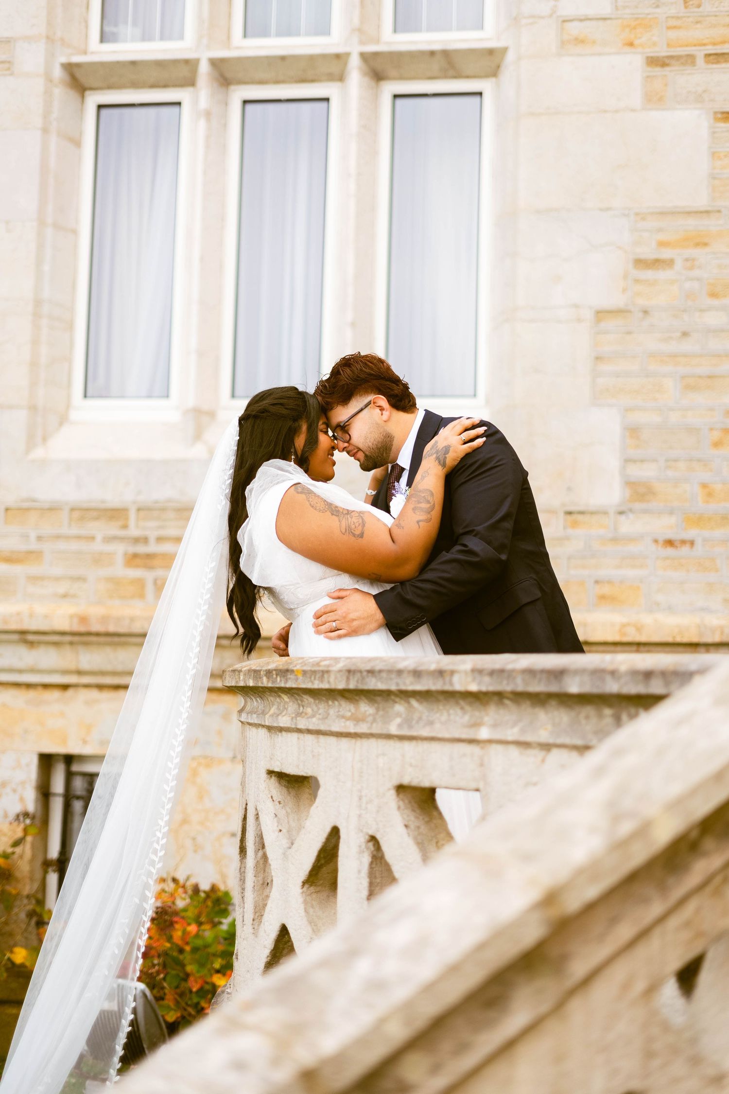 A romantic wedding couple shares an intimate moment on a stone balcony of a historic building.