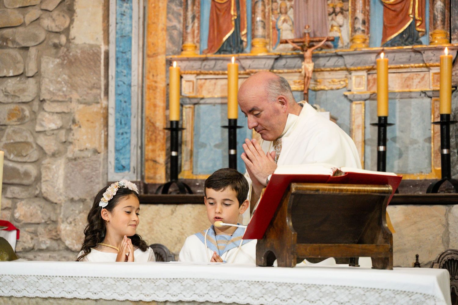Children participate in a religious ceremony with a priest at a church altar.