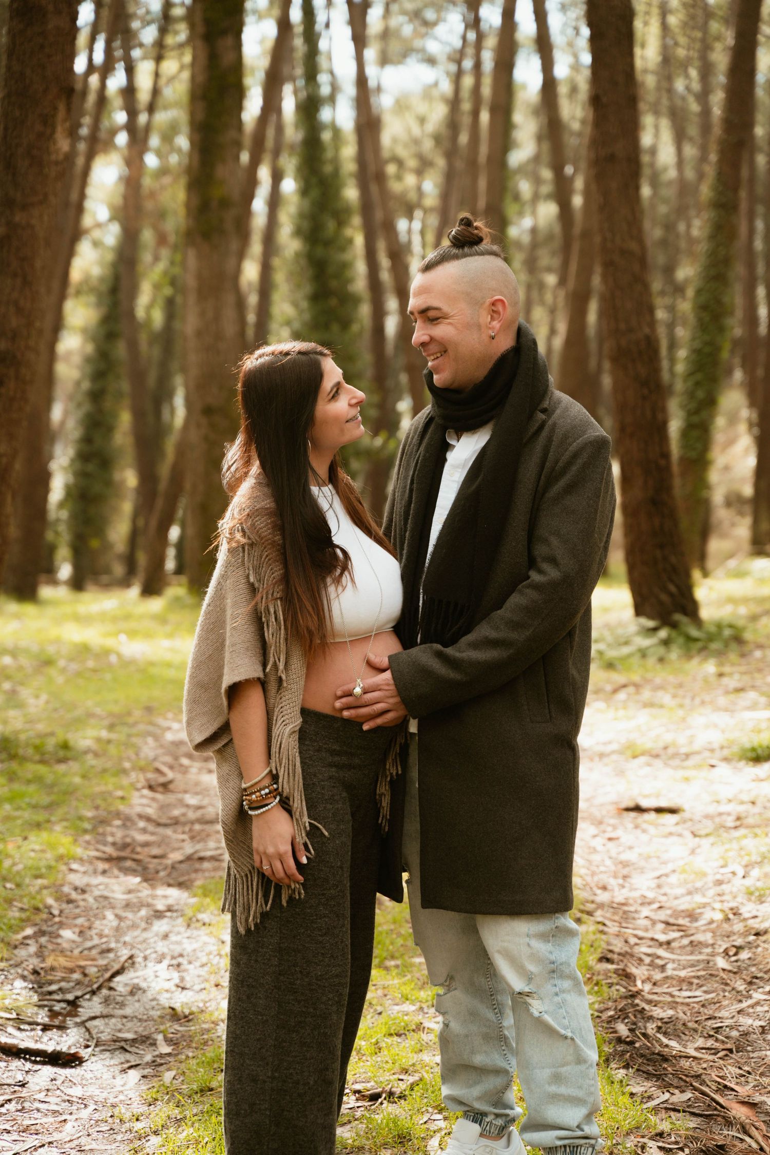 Expectant couple sharing an intimate moment together in a sunlit forest setting.