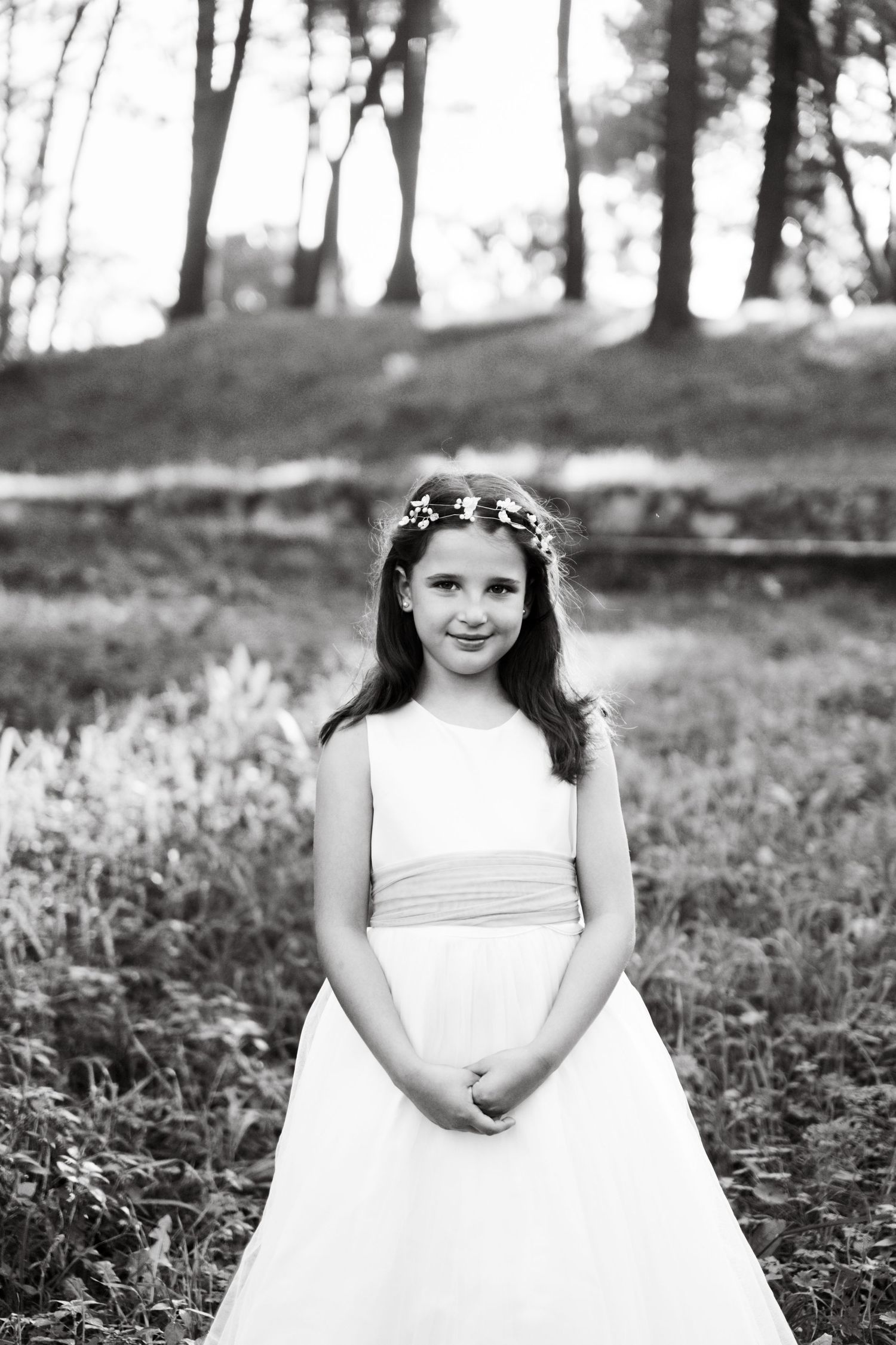 Black and white portrait in a woodland setting featuring an elegant white dress and floral crown.
